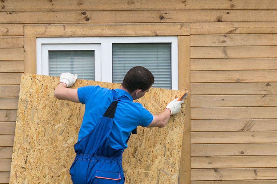 Hurricane Preparedness - Man in Gloves and Coveralls Boards up a Home's Windows, Preparing for a Storm